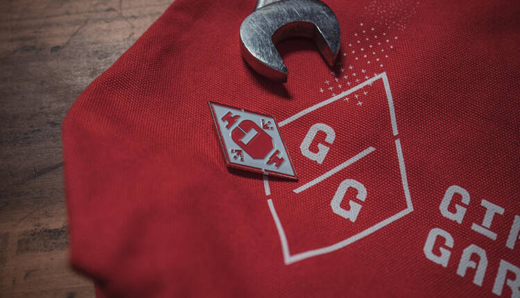 Logo with enamel pin and wrench laying on a red canvas tote bag